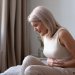 Endometriosis is a chronic and often debilitating inflammatory disease, affecting 1 in 7 Australian women. Image: Adobe. A woman in pain sitting on her bed clutching her stomach.